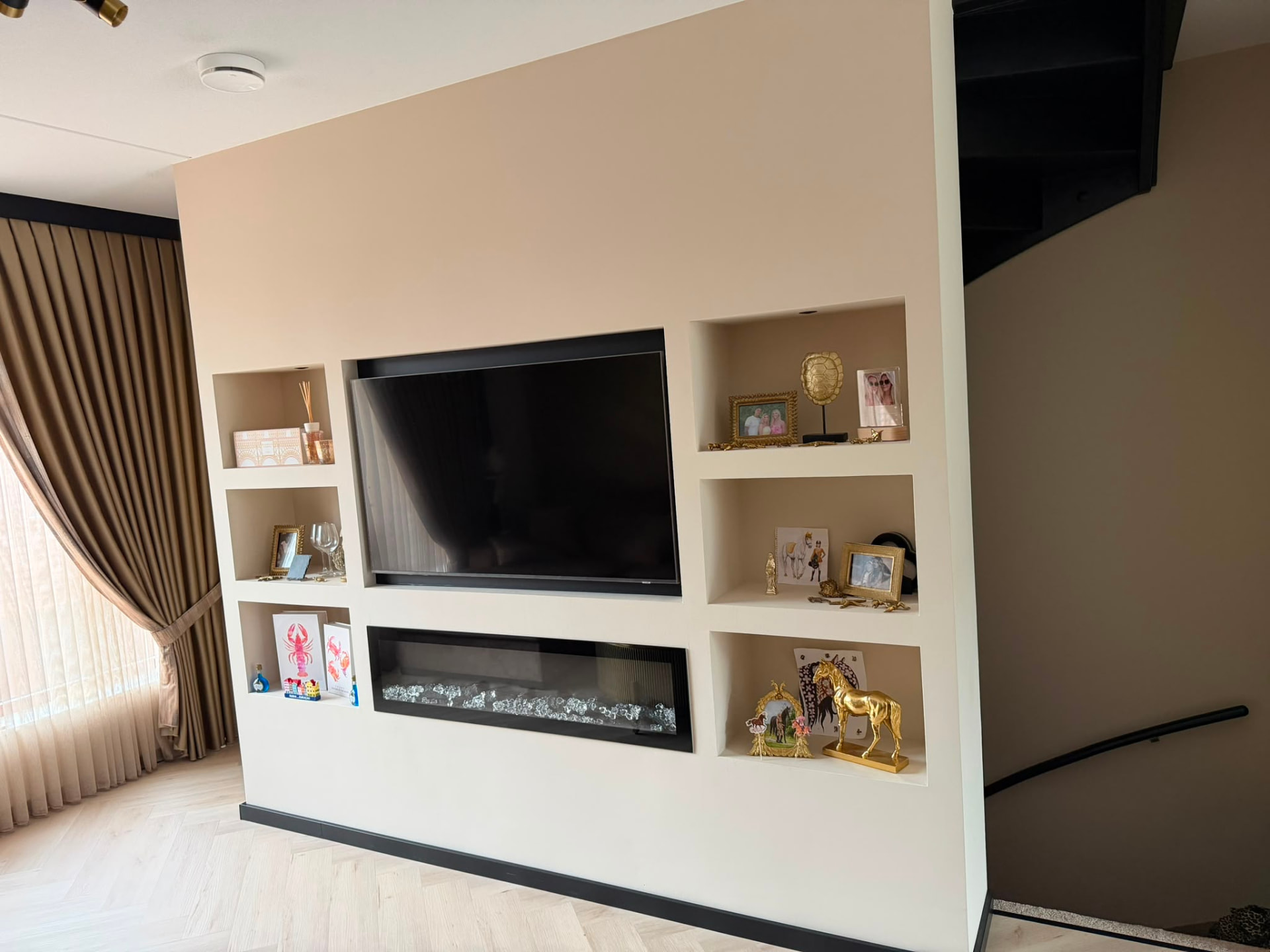 Creamwitte maatwerkwand met televisie en zicht op de woonkamer